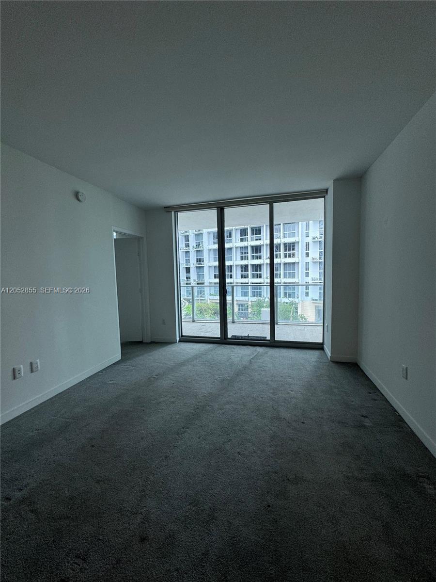 An empty room features gray carpeting, white walls, and a large sliding glass door — 1100 S Miami Ave # 411, Miami FL 33130, MIAMI, FL