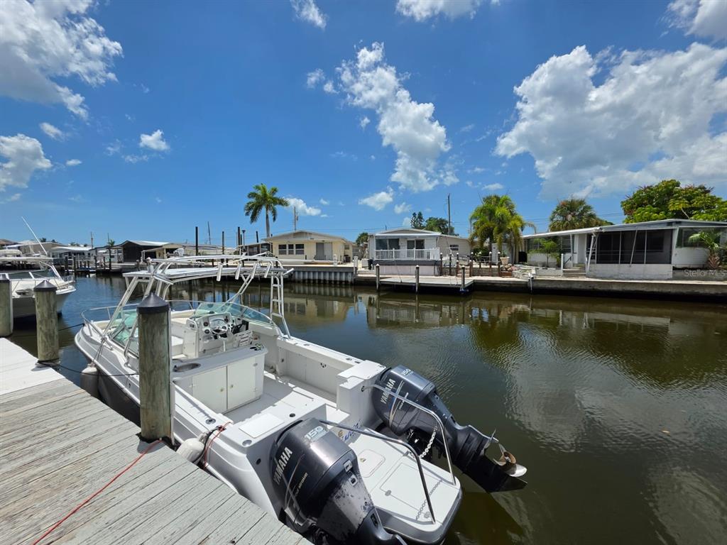 A white motorboat with twin Yamaha engines is docked in a canal near several homes — 1714 69TH AVENUE W UNIT A204, BRADENTON, FL