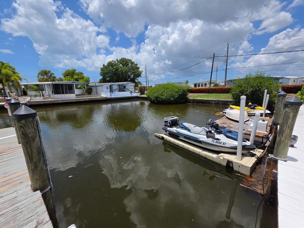 A canal view featuring a wooden dock with two jet skis and nearby mobile homes — 1714 69TH AVENUE W UNIT A204, BRADENTON, FL