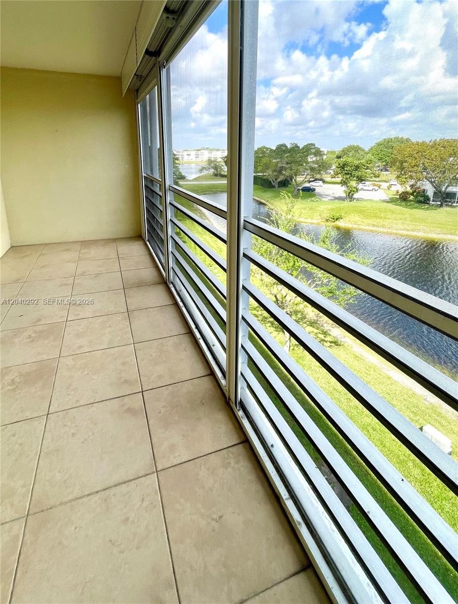 A screened-in balcony features beige tile flooring and views of a lake and trees — 4031 Harwood D # 4031, Deerfield Beach FL 33442, DEERFIELD BEACH, FL