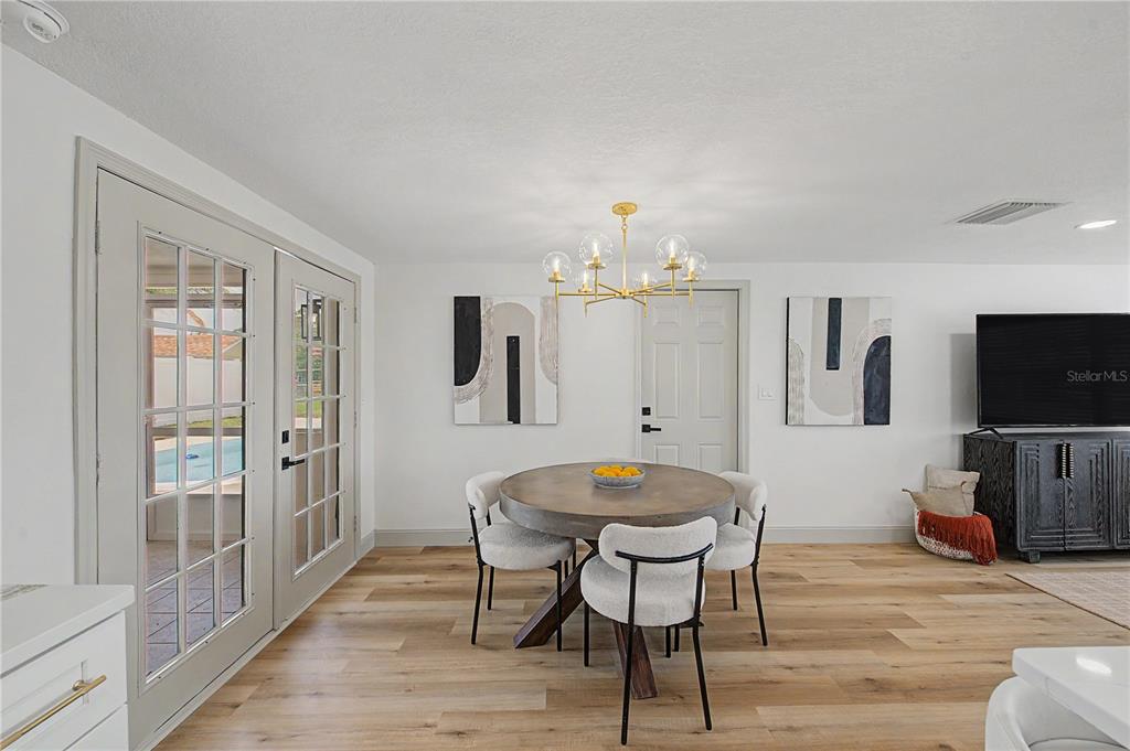 A dining area features a round wooden table, four chairs, and a modern gold chandelier — 2619 ALBION STREET, HOLIDAY, FL