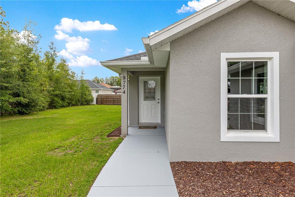 A gray stucco house exterior features a white front door and a concrete walkway — 8774 SE 162ND STREET, SUMMERFIELD, FL