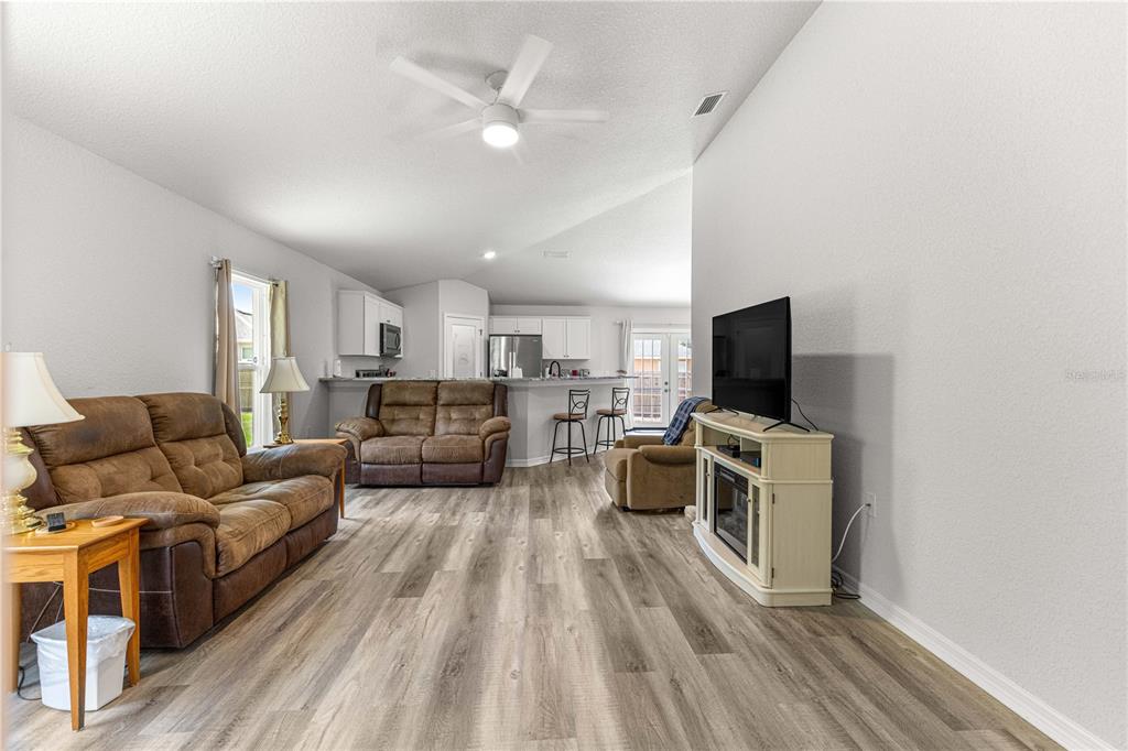 A living room with wood-look flooring, a ceiling fan, and an open kitchen beyond — 8774 SE 162ND STREET, SUMMERFIELD, FL