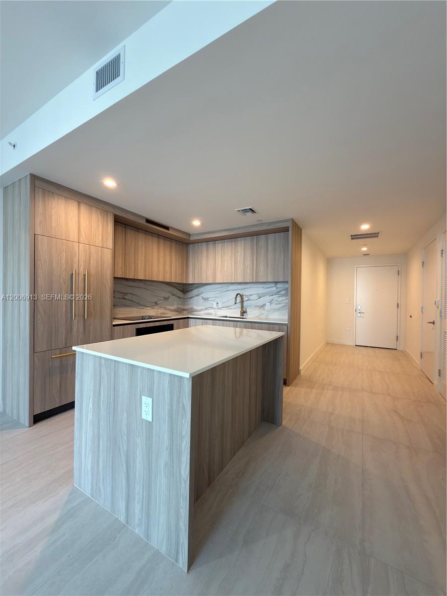 A modern kitchen features wood-grain cabinetry, a white quartz island, and light tile flooring — 77 SE 5th St # 1602, Miami FL 33131, MIAMI, FL