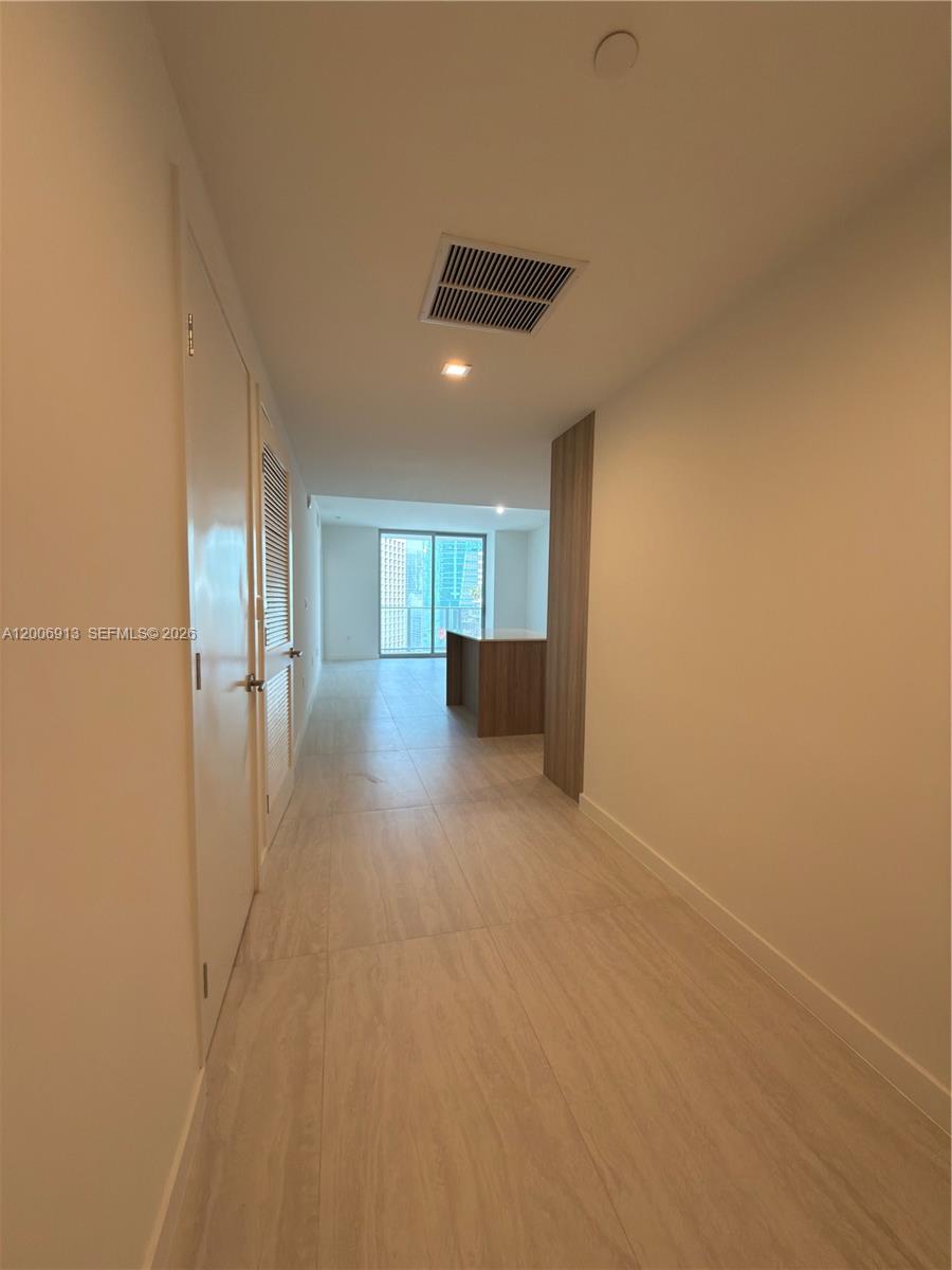 A hallway with light tile flooring leads toward a living area with floor-to-ceiling windows — 77 SE 5th St # 1602, Miami FL 33131, MIAMI, FL