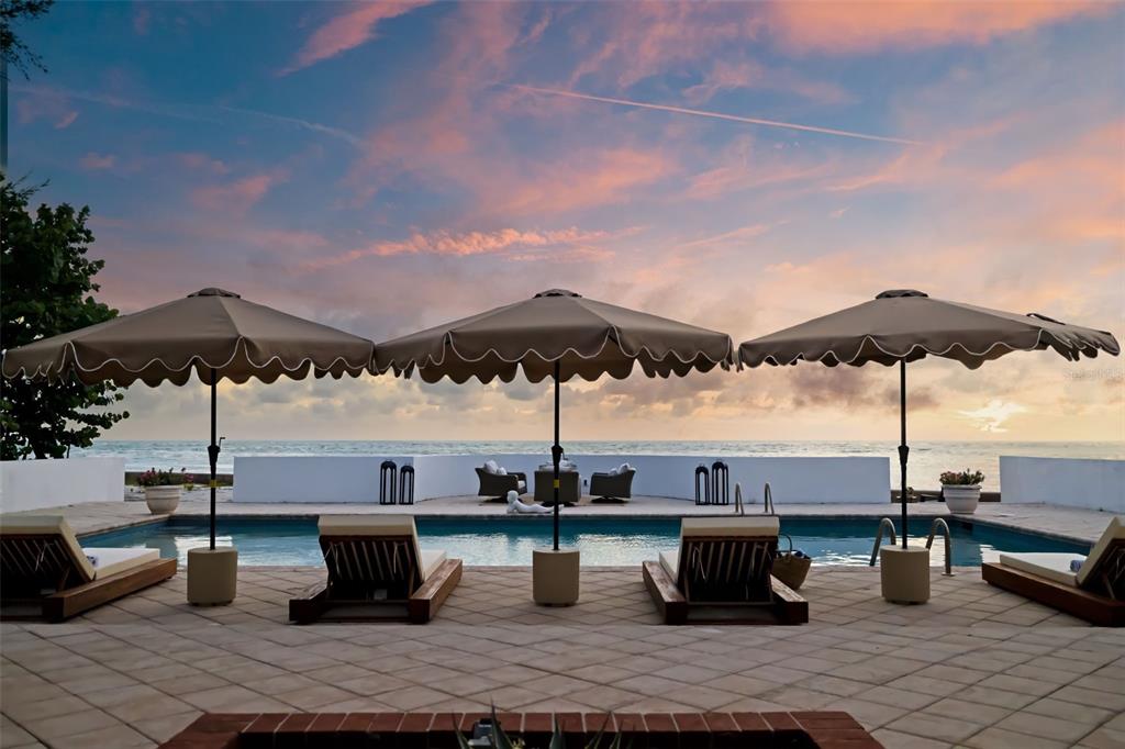 A swimming pool patio features three umbrellas, lounge chairs, and a view of the ocean — 1157 WESTWAY DRIVE, SARASOTA, FL