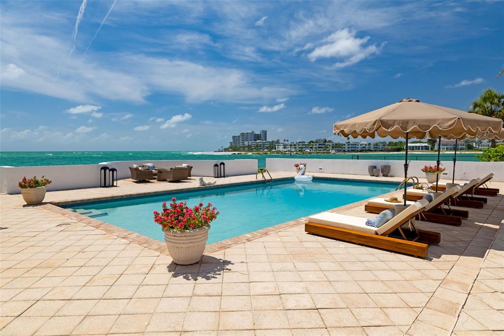 A swimming pool with lounge chairs and an umbrella overlooks the ocean — 1157 WESTWAY DRIVE, SARASOTA, FL
