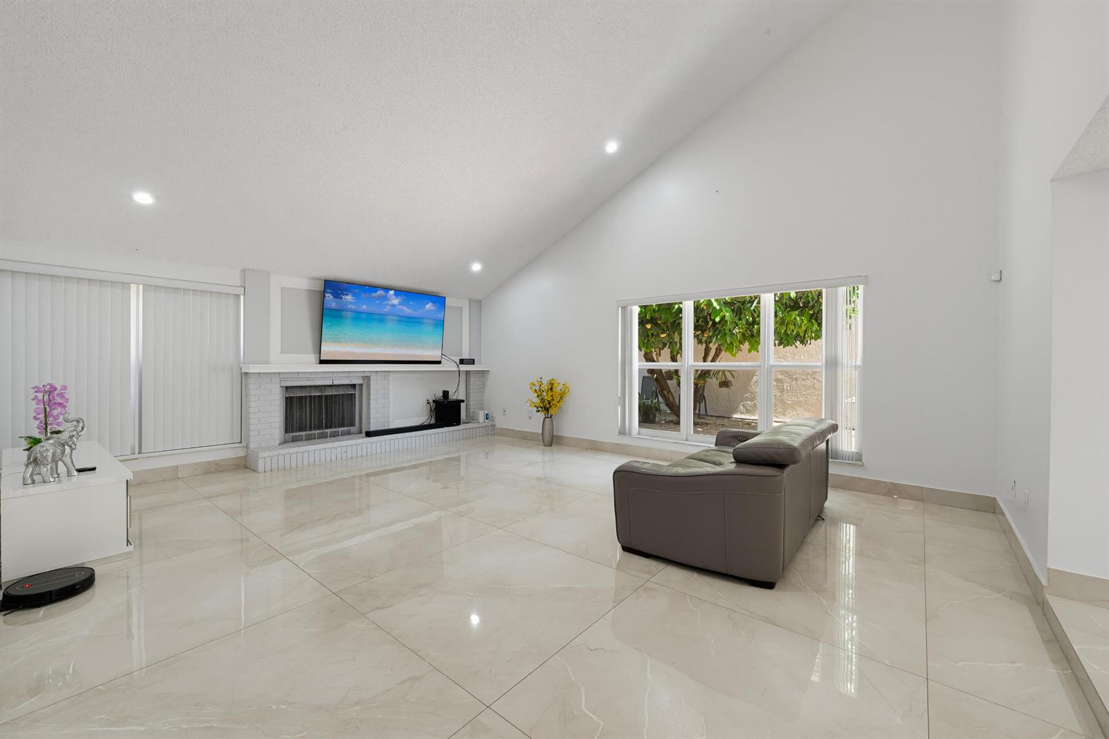 A living room with white walls, vaulted ceilings, large tile flooring, and a brick fireplace — 8811 SW 150th Place Circle, Miami FL 33196, MIAMI, FL