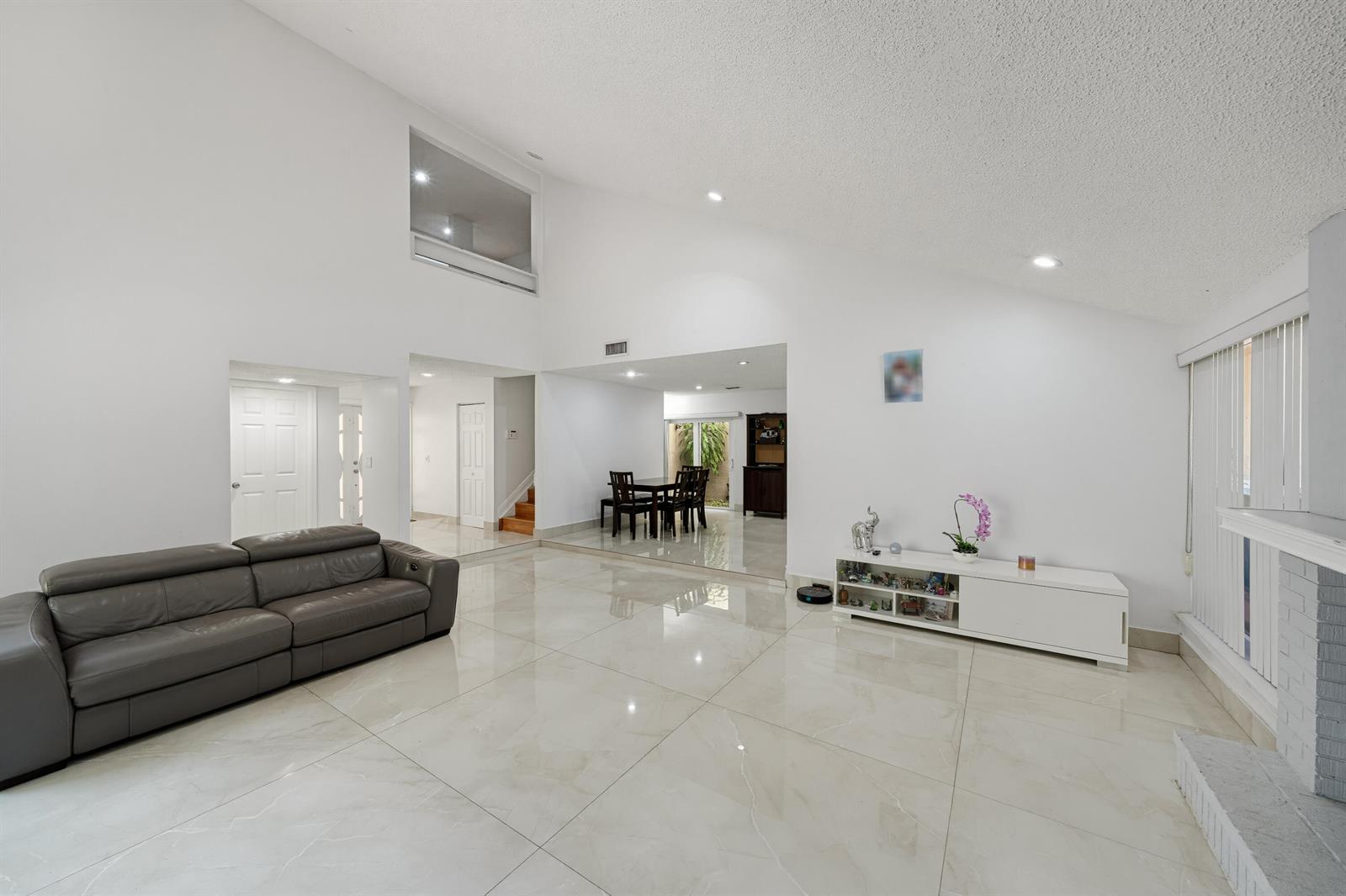 A spacious living room features white tiled floors, high ceilings, and a dark leather sofa — 8811 SW 150th Place Circle, Miami FL 33196, MIAMI, FL