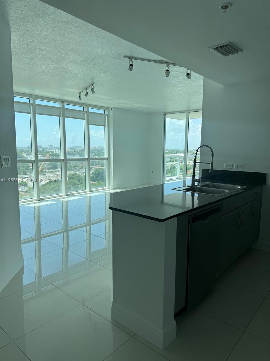 A modern kitchen with a dark countertop and sink overlooks a bright living area — 1871 NW S River Dr # 1503, Miami FL 33125, MIAMI, FL