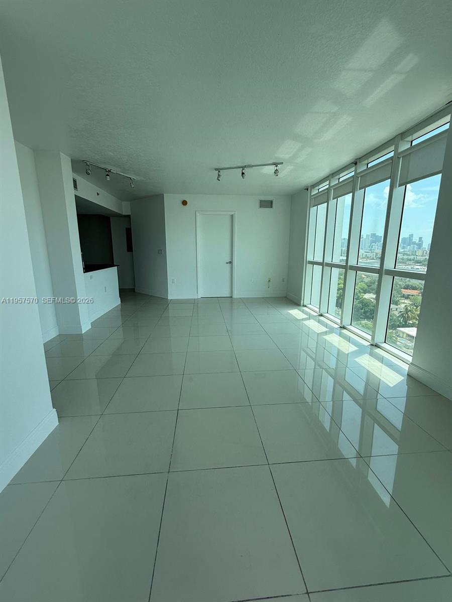 An empty living room features white tile floors, track lighting, and floor-to-ceiling windows — 1871 NW S River Dr # 1503, Miami FL 33125, MIAMI, FL