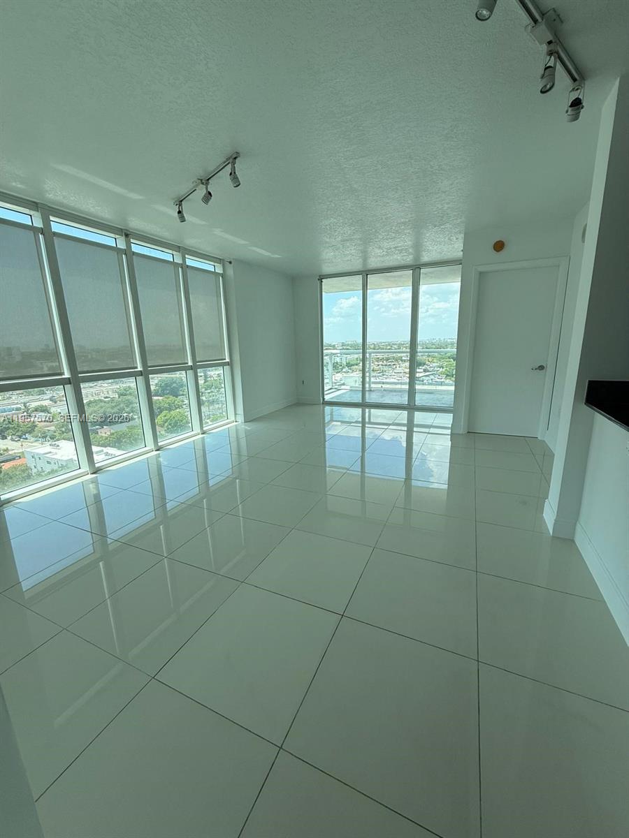 A bright, empty room features white tile floors, floor-to-ceiling windows, and a balcony view — 1871 NW S River Dr # 1503, Miami FL 33125, MIAMI, FL
