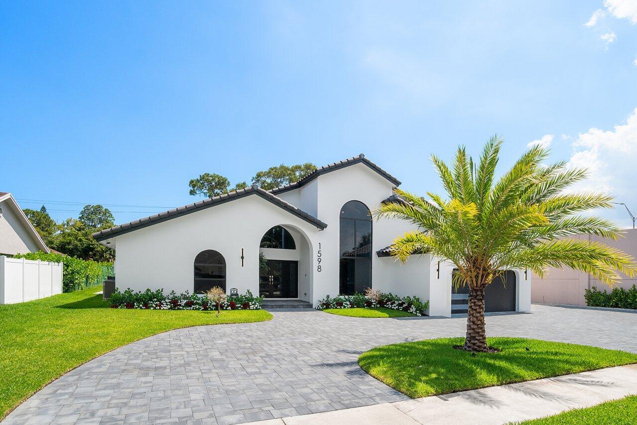 A white single-story house with a paved driveway, arched windows, and a palm tree — 1598 SW 17th Street, Boca Raton FL 33486, BOCA RATON, FL