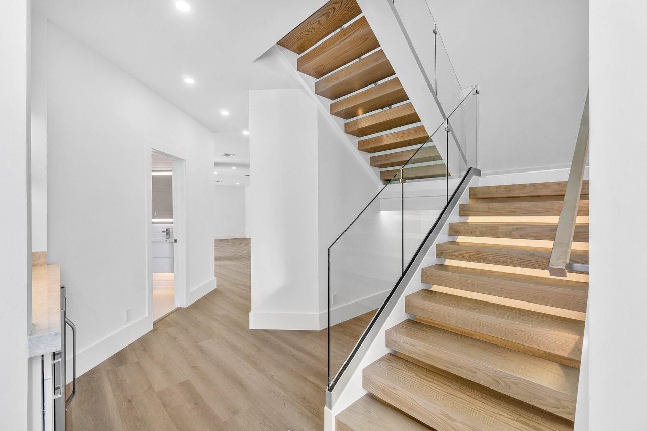A modern staircase with wooden treads and a glass railing leads to an upper floor — 1598 SW 17th Street, Boca Raton FL 33486, BOCA RATON, FL
