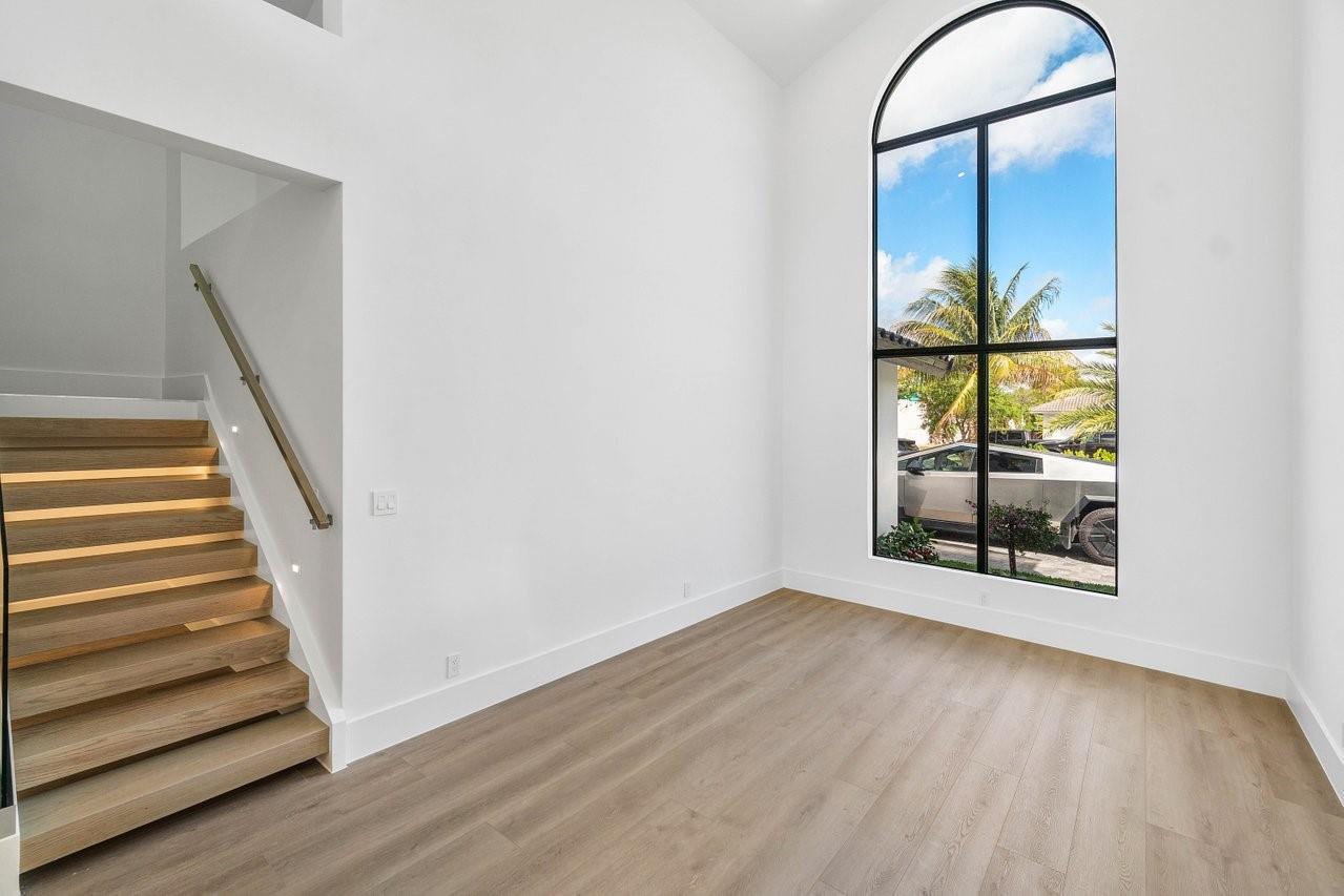 A bright room with light wood flooring, a floating staircase, and a tall arched window — 1598 SW 17th Street, Boca Raton FL 33486, BOCA RATON, FL