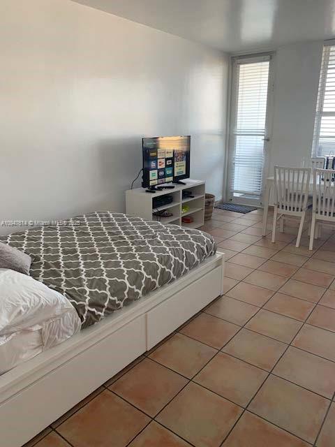 A bedroom features a bed with a patterned duvet, a television stand, and tile flooring — 100 Lincoln Rd # 1219, Miami Beach FL 33139, MIAMI BEACH, FL