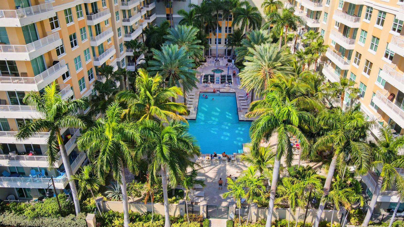 An aerial view shows a swimming pool surrounded by palm trees and multi-story apartment buildings — 700 E Boynton Beach Boulevard # 608, Boynton Beach FL 33435, BOYNTON BEACH, FL