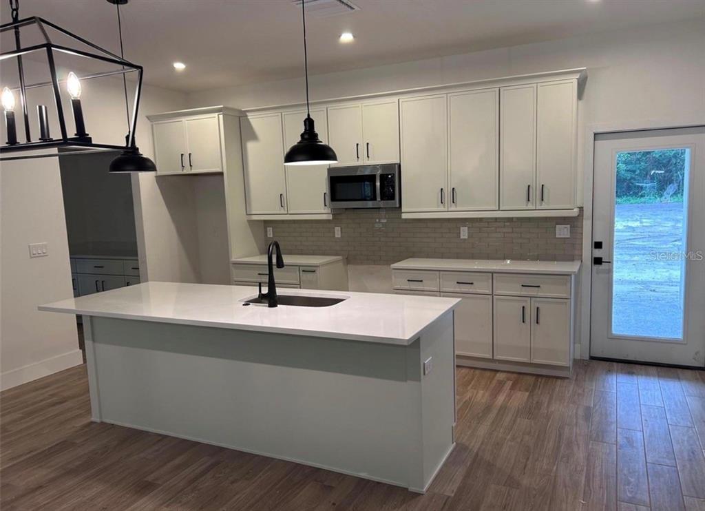 A modern kitchen features a white island, light-colored cabinetry, stainless steel appliances, and wood flooring — 330 KIMBLE AVENUE, OVIEDO, FL