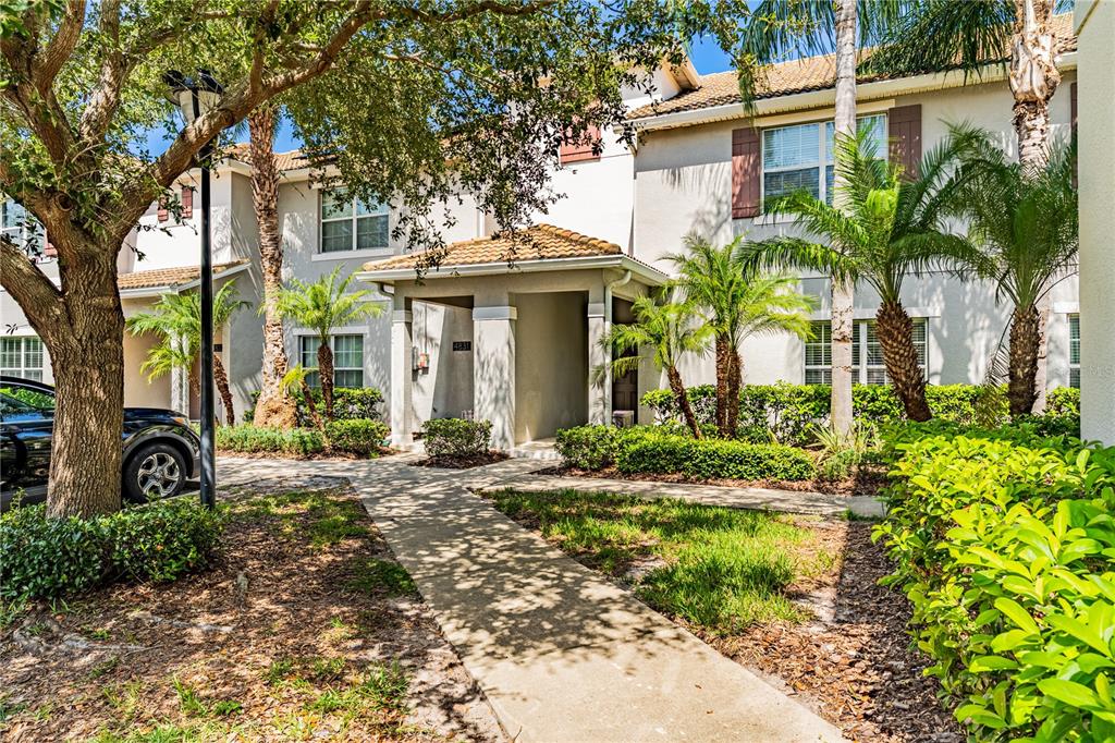 A concrete walkway leads to the covered entrance of a two-story tan stucco townhouse — 4827 CLOCK TOWER DRIVE, KISSIMMEE, FL