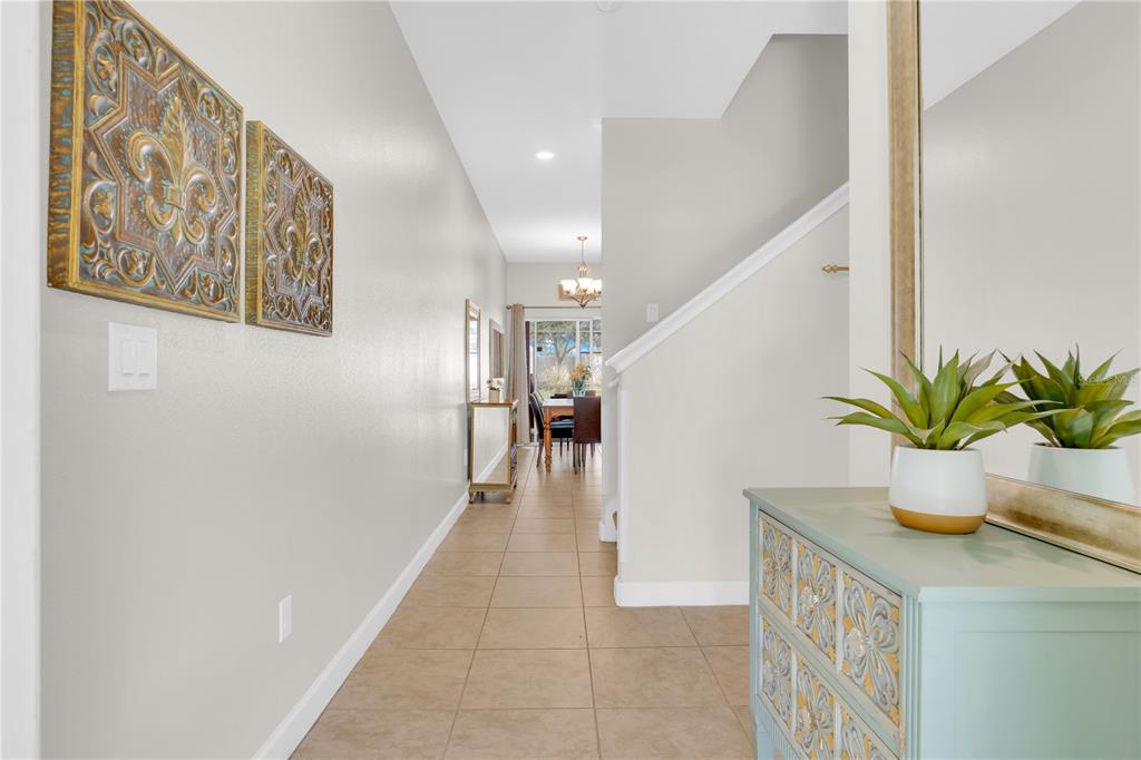 A tiled hallway leads past a staircase toward a dining area with a large mirror — 4827 CLOCK TOWER DRIVE, KISSIMMEE, FL