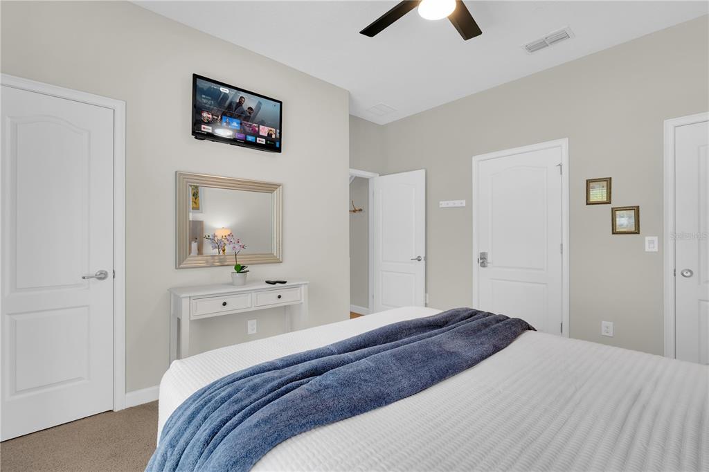 A bedroom features a white console table, a wall-mounted television, and a bed with a blue throw — 4827 CLOCK TOWER DRIVE, KISSIMMEE, FL
