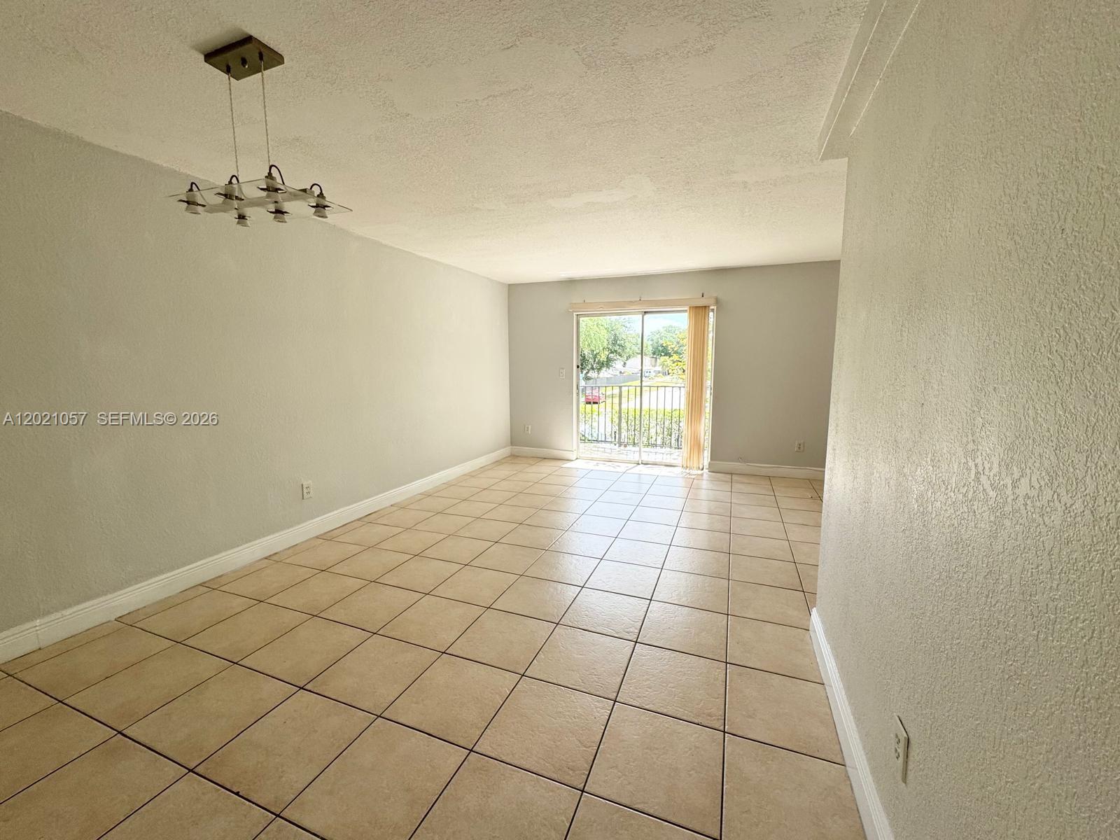 An empty living room features light-colored tile flooring, gray walls, and a sliding glass door — 8600 SW 109th Ave # 202, Miami FL 33173, MIAMI, FL