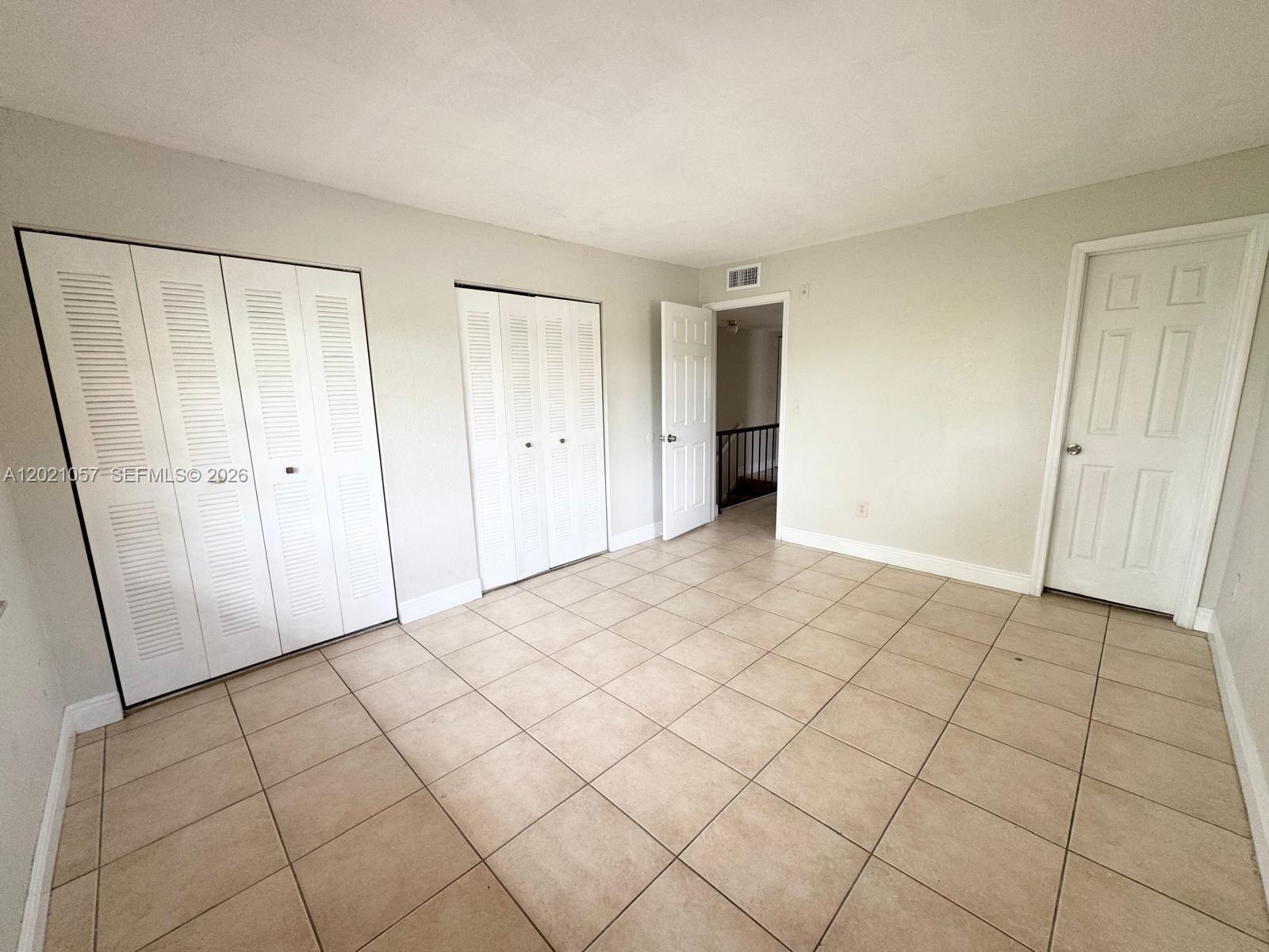 An empty bedroom features light-colored walls, beige tile flooring, two sets of closet doors, and two interior doors — 8600 SW 109th Ave # 202, Miami FL 33173, MIAMI, FL