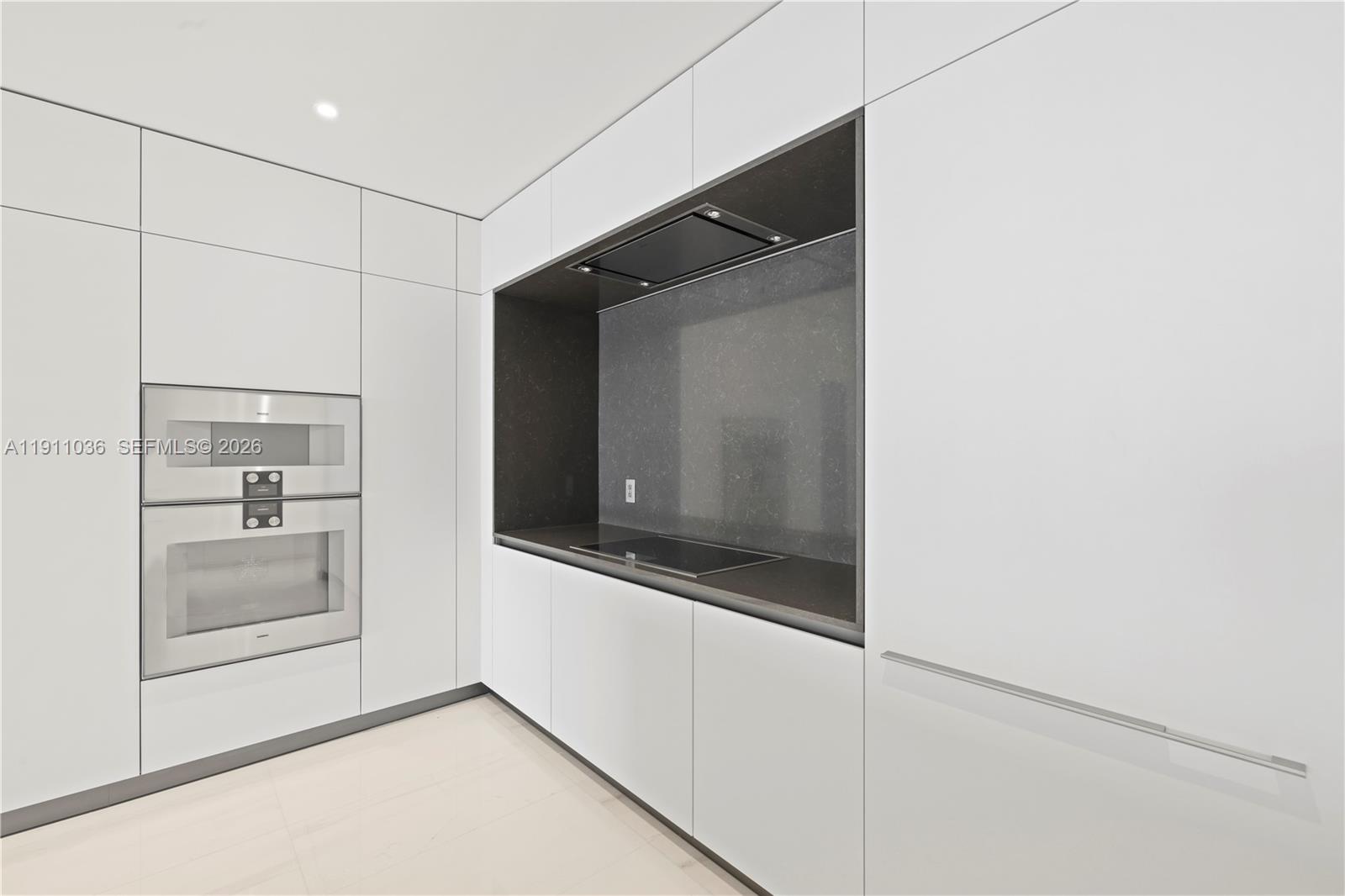 A modern kitchen features white cabinetry, stainless steel appliances, and a dark stone backsplash — 300 Biscayne Blvd Way # 3404, Miami FL 33131, MIAMI, FL