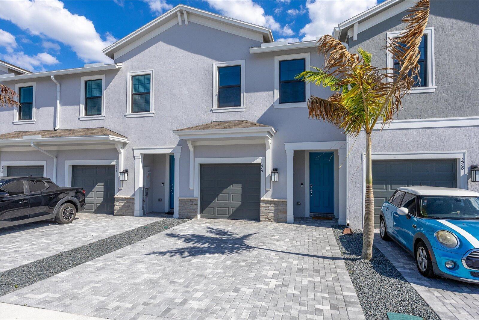A row of three-story townhomes with gray stucco facades, blue front doors, and paved driveways — 276 SW Sally Way, Stuart FL 34997, STUART, FL