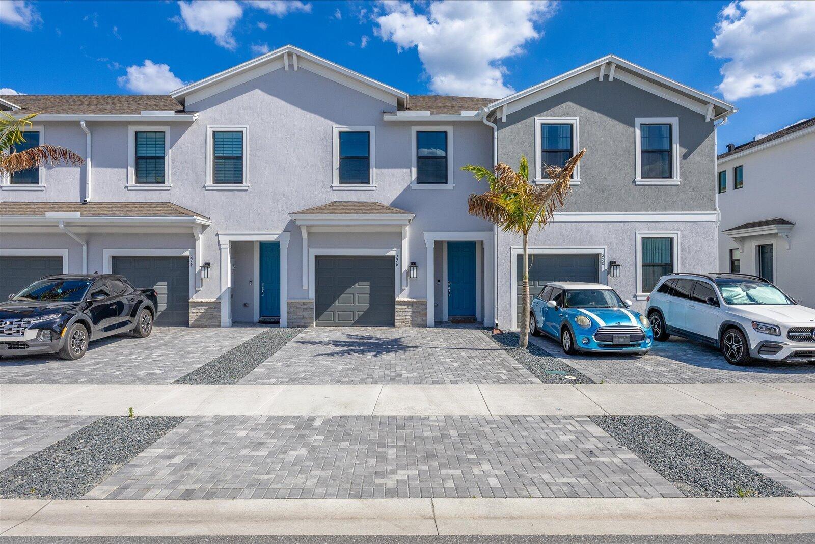 A row of three modern townhouses with paved driveways and parked cars under a blue sky — 276 SW Sally Way, Stuart FL 34997, STUART, FL