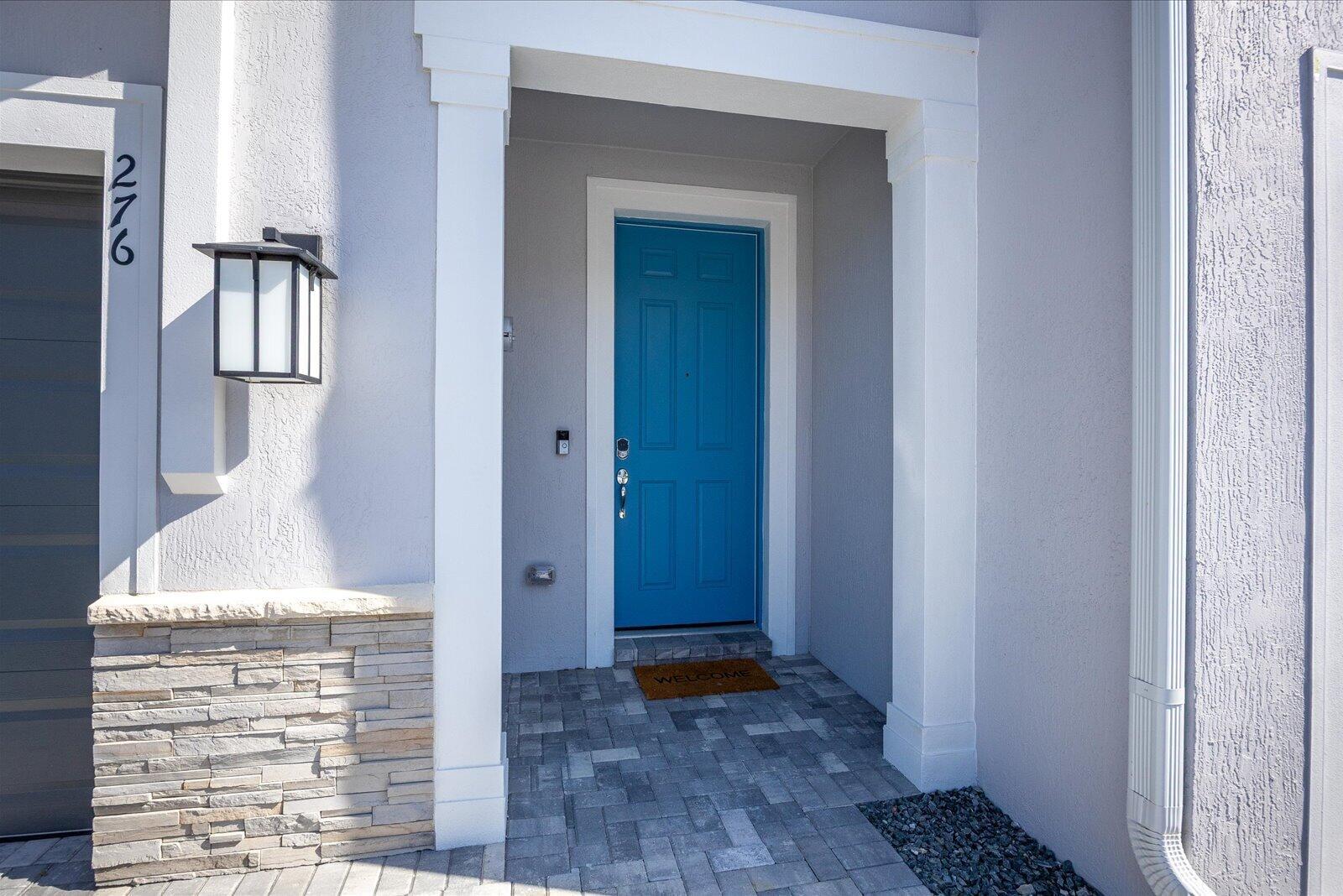 A bright blue front door is centered within a covered entryway with stone accents — 276 SW Sally Way, Stuart FL 34997, STUART, FL