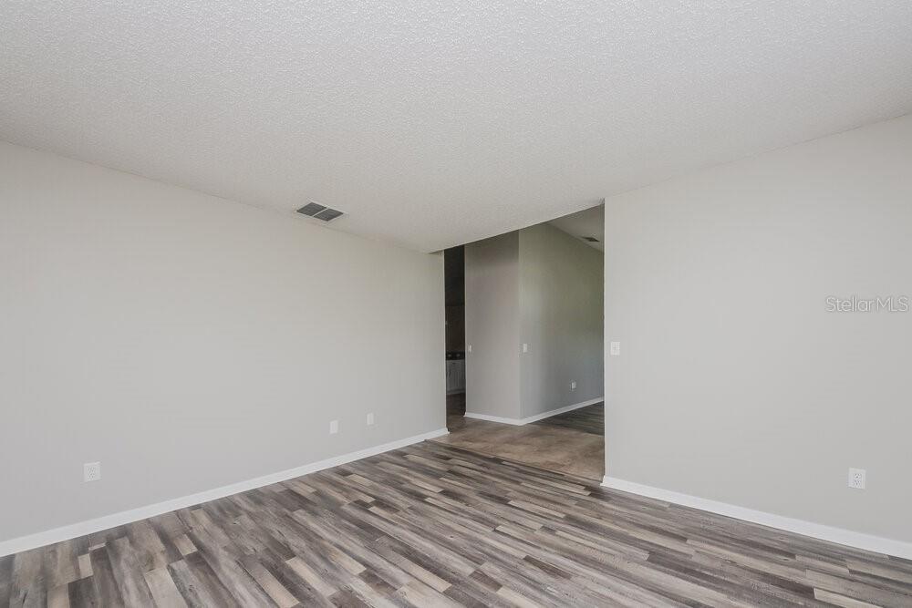 An empty room with light gray walls and wood-look laminate flooring leads to a hallway — 46 DORSET DRIVE, KISSIMMEE, FL