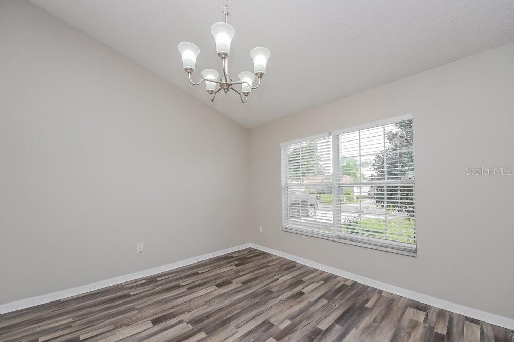 An empty dining room features light gray walls, wood-look flooring, and a multi-light chandelier — 46 DORSET DRIVE, KISSIMMEE, FL
