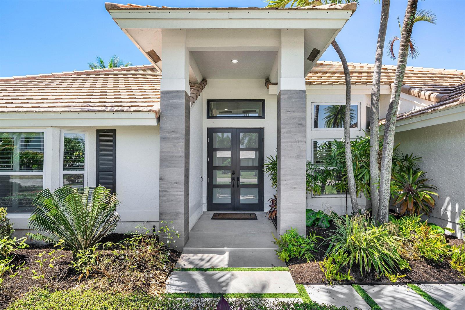 The exterior of a house features a covered entryway with double glass doors and palm trees — 916 SW 37th Court, Boynton Beach FL 33435, BOYNTON BEACH, FL