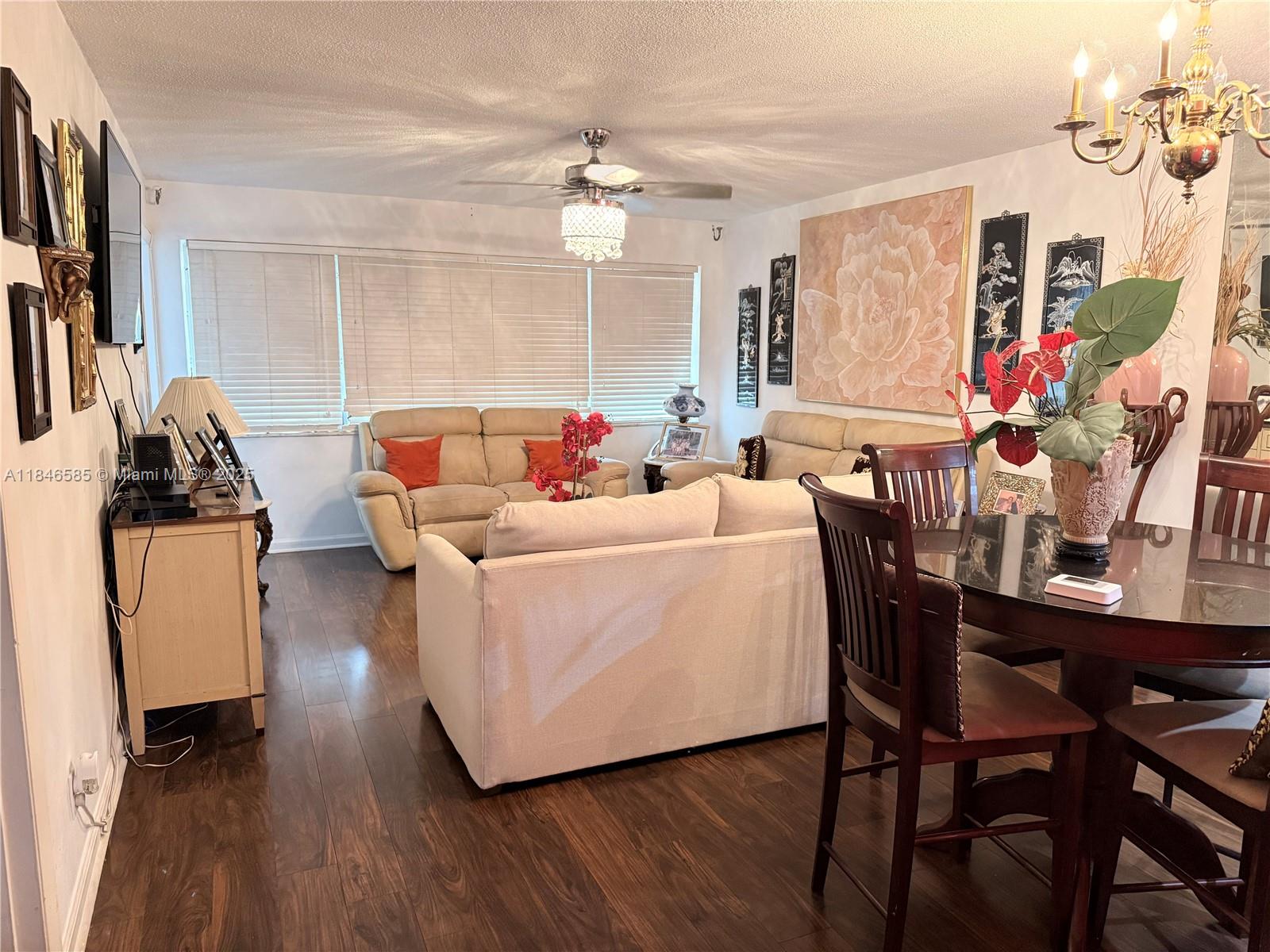 A living and dining room area features dark wood flooring, beige sofas, and a chandelier — 215 SE 3rd Ave # 102C, Hallandale Beach FL 33009, HALLANDALE BEACH, FL