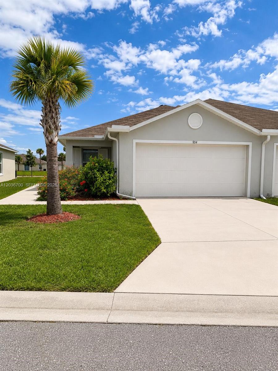 A single-story house with a white garage door, a palm tree, and a green lawn — 9114 Aegean Cir, Lehigh Acres FL 33936, LEHIGH ACRES, FL