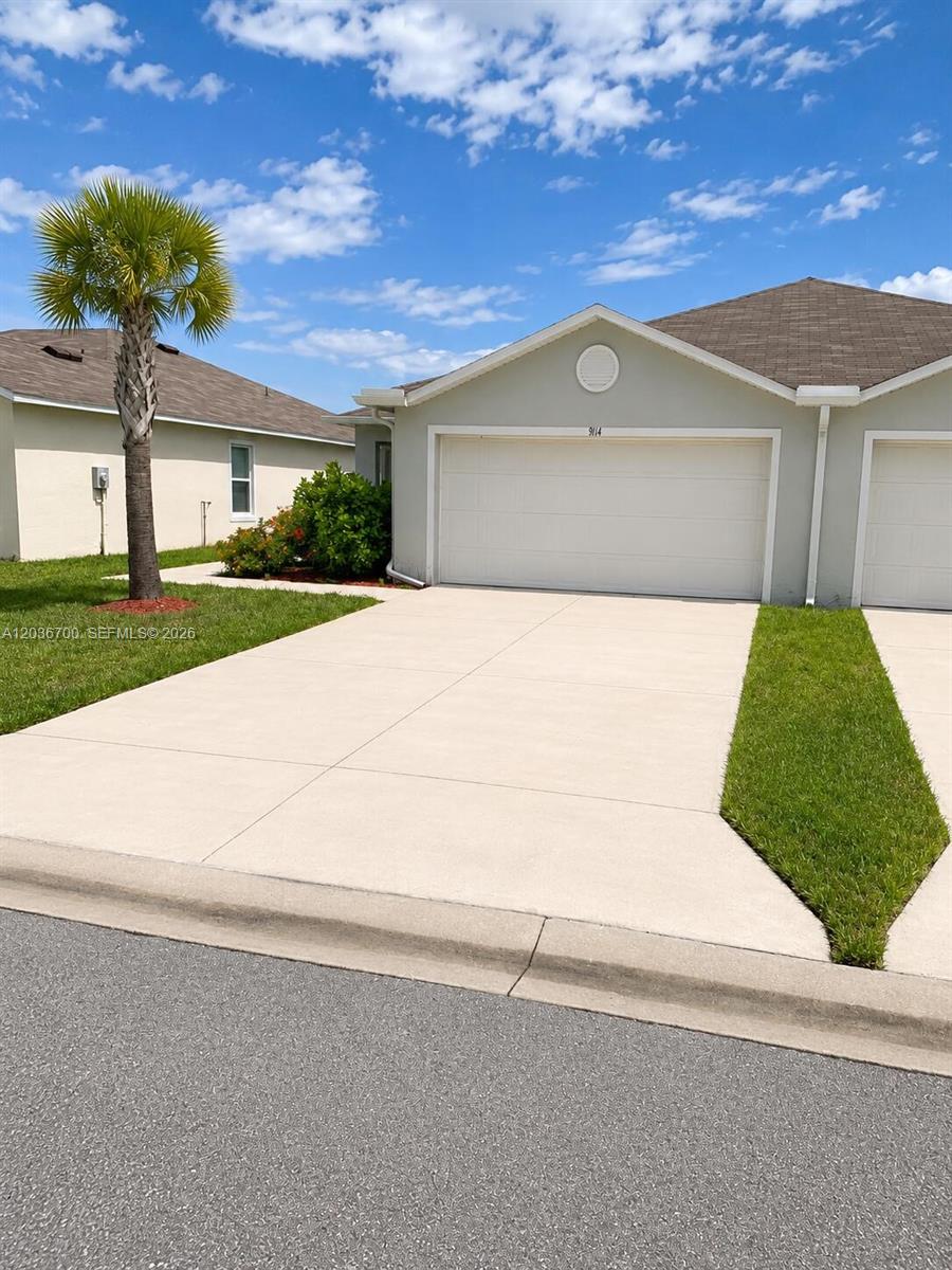 A single-story house with a two-car garage, a concrete driveway, and a palm tree — 9114 Aegean Cir, Lehigh Acres FL 33936, LEHIGH ACRES, FL