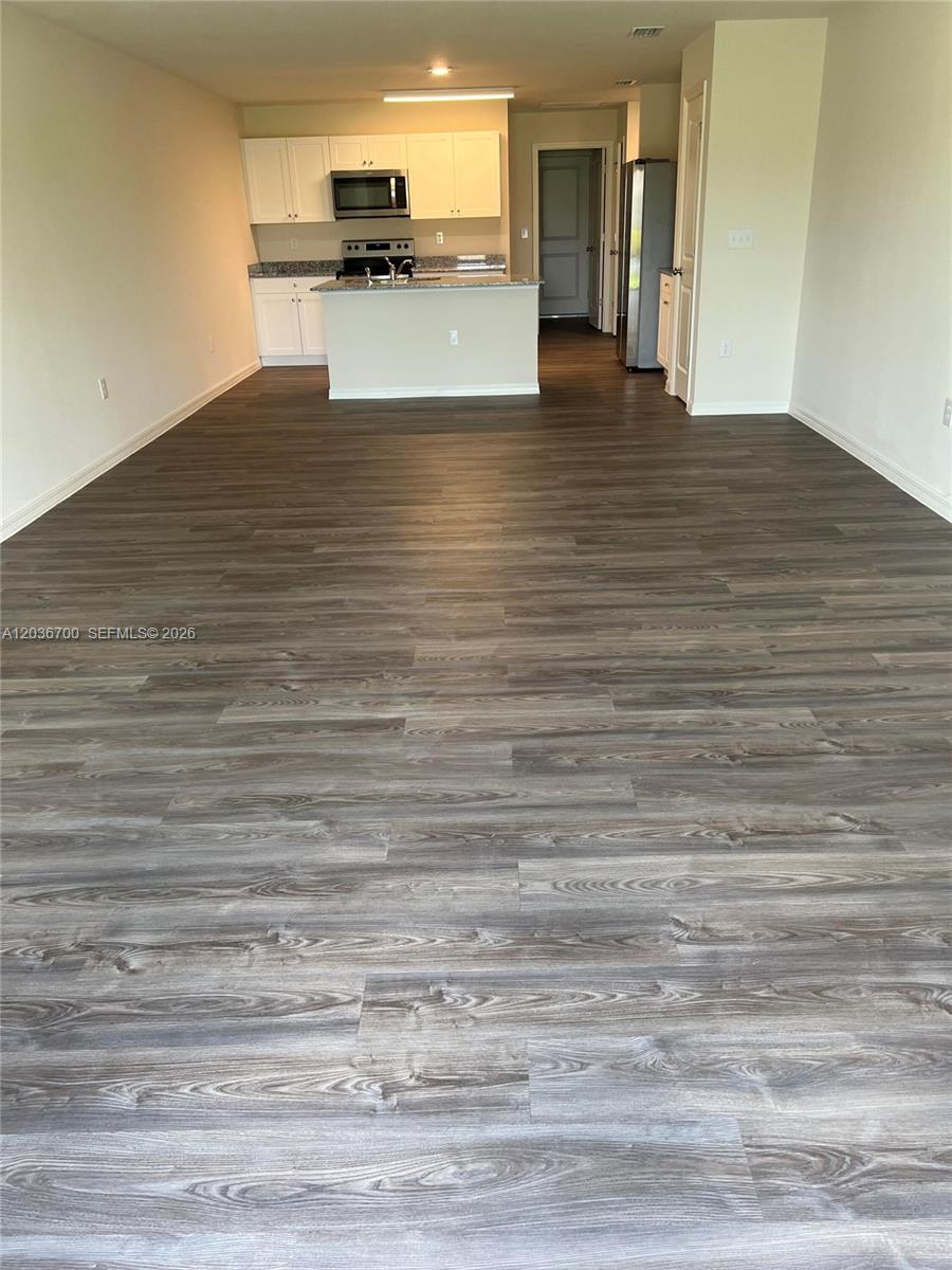 An open-concept kitchen features white cabinetry, granite countertops, and wood-look flooring — 9114 Aegean Cir, Lehigh Acres FL 33936, LEHIGH ACRES, FL
