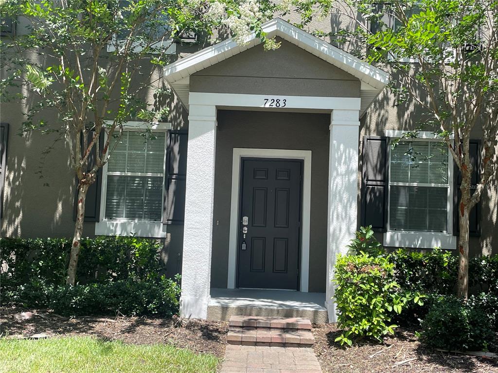 A dark front door with a keypad lock is centered under a covered entryway — 7283 PENKRIDGE LANE, WINDERMERE, FL