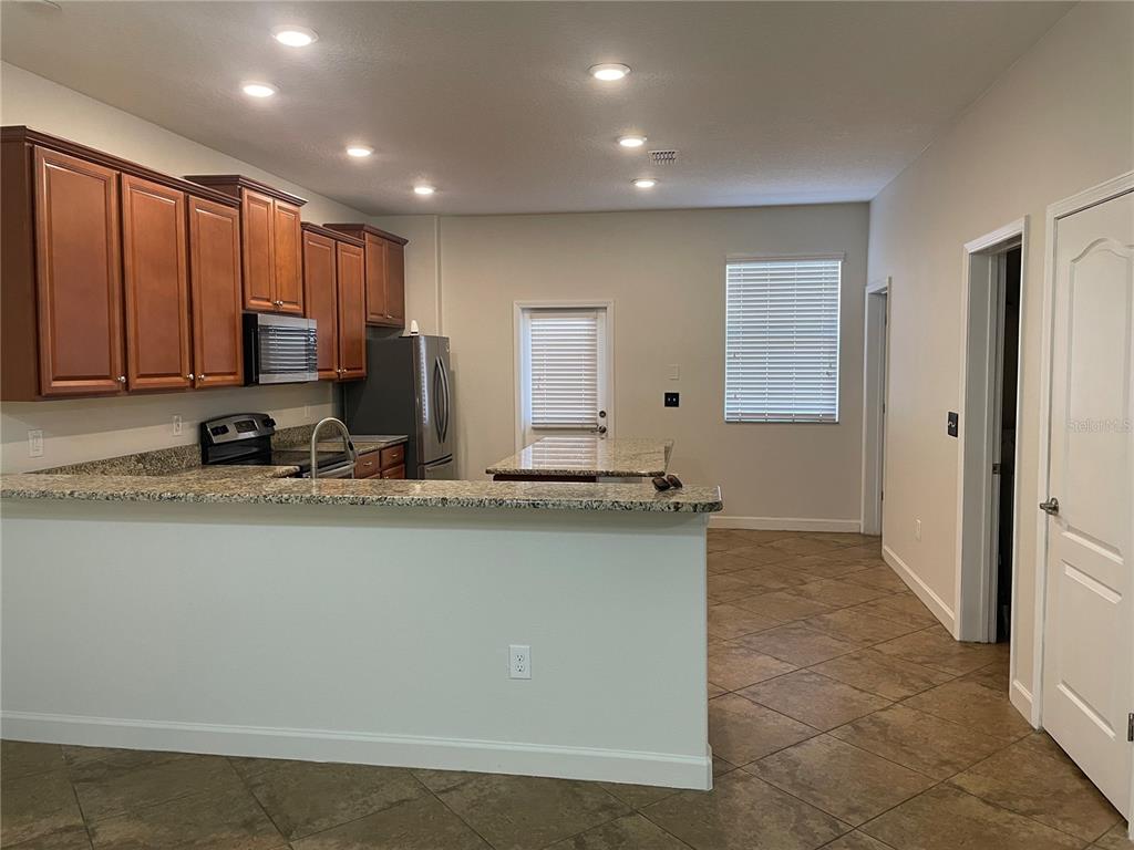 A kitchen features wood cabinets, granite countertops, stainless steel appliances, and tile flooring — 7283 PENKRIDGE LANE, WINDERMERE, FL
