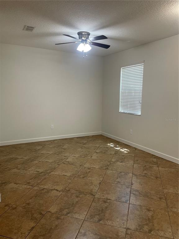 An empty room with tan tile flooring, white walls, and a ceiling fan — 7283 PENKRIDGE LANE, WINDERMERE, FL