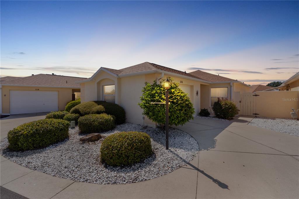 A single-story house with a beige exterior, a concrete driveway, and landscaped front yard bushes — 1116 SAN BERNARDO ROAD, THE VILLAGES, FL