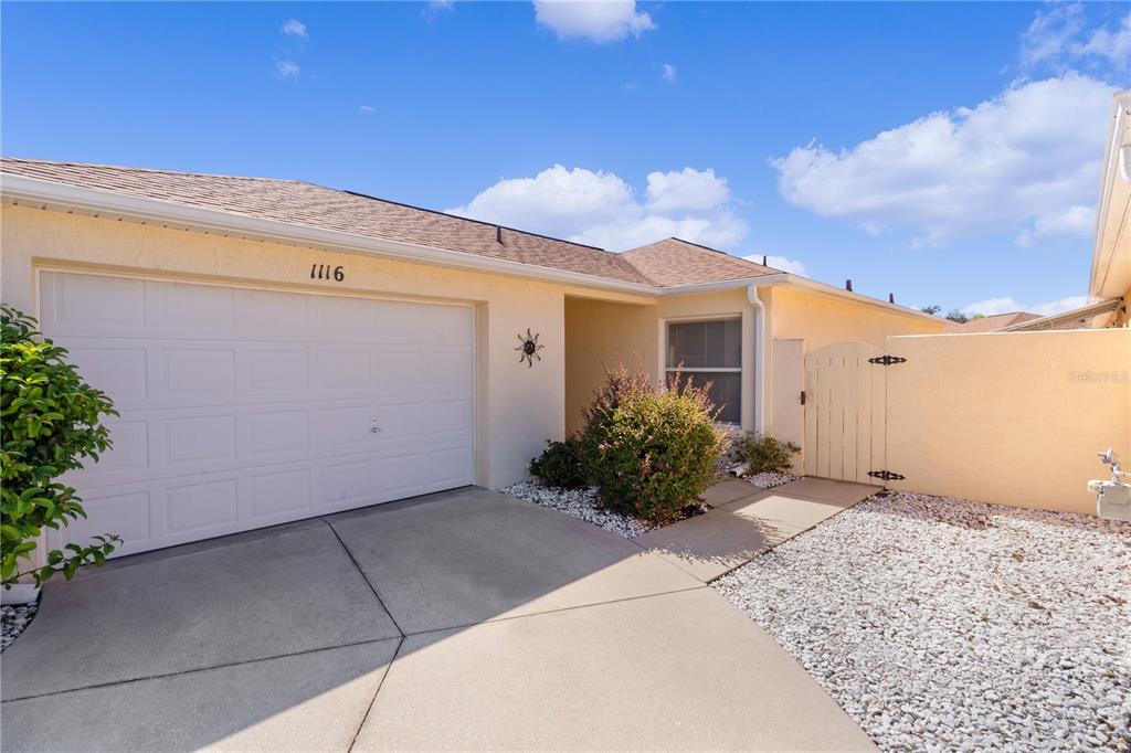 A single-story house exterior features a white garage door, a concrete driveway, and a gate — 1116 SAN BERNARDO ROAD, THE VILLAGES, FL