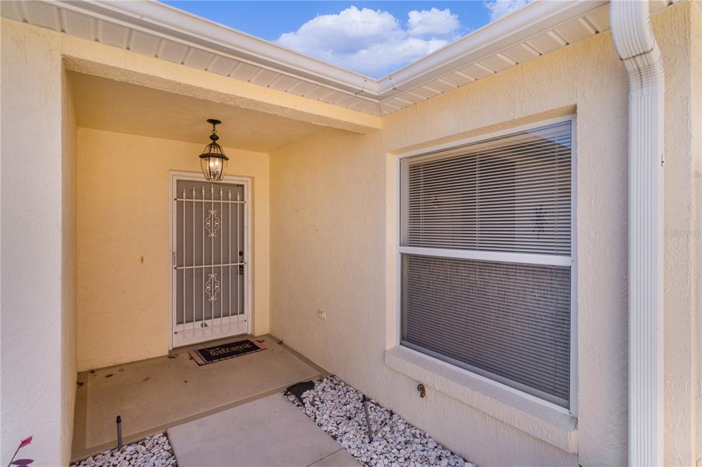 A covered entryway features a white storm door, a welcome mat, and a large window — 1116 SAN BERNARDO ROAD, THE VILLAGES, FL