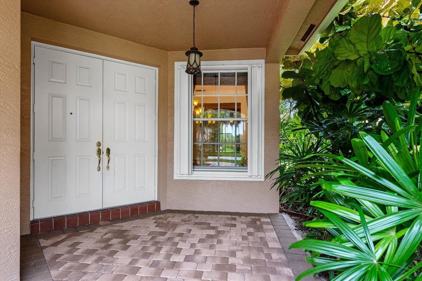A white double door entrance with a window and brick paver porch surrounded by plants — 8882 Hidden Acres Drive, Boynton Beach FL 33473, BOYNTON BEACH, FL