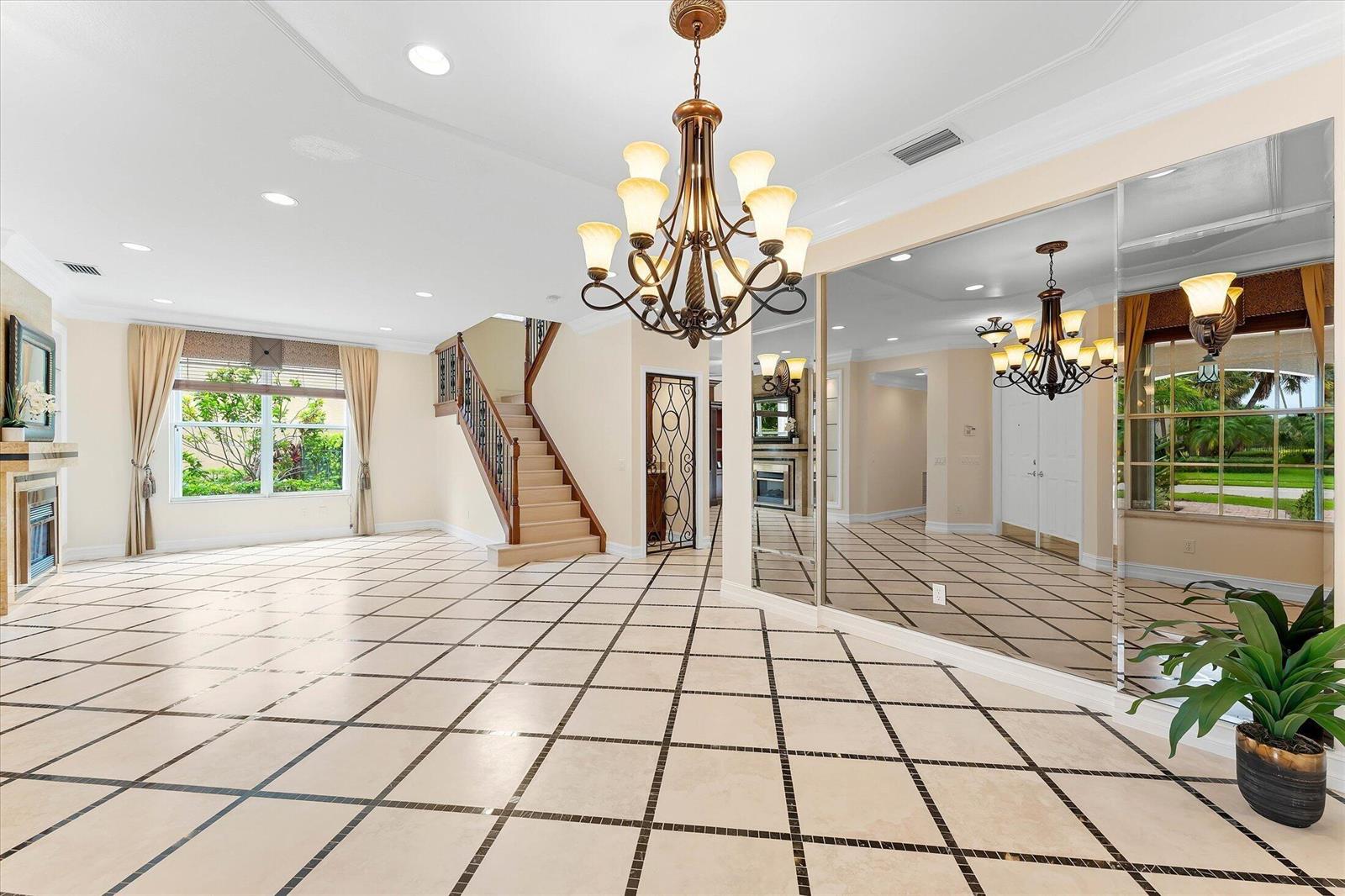 A spacious living room features a large chandelier, tiled floors, a staircase, and mirrored walls — 8882 Hidden Acres Drive, Boynton Beach FL 33473, BOYNTON BEACH, FL