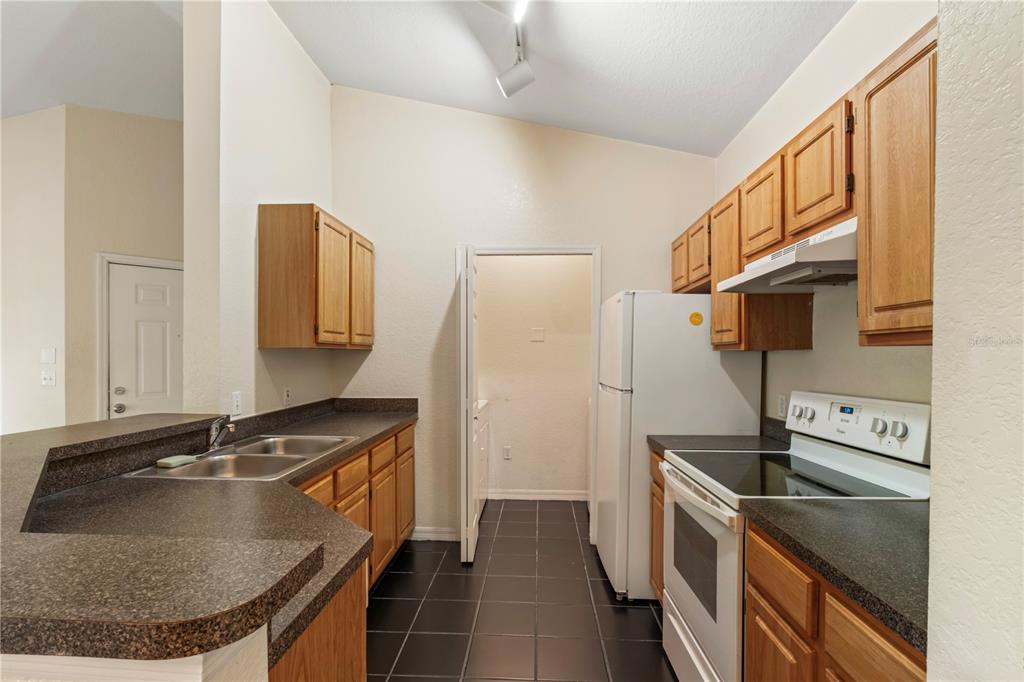 A kitchen features wood cabinets, dark countertops, black tile flooring, and white appliances — 6025 WESTGATE DRIVE UNIT 2533, ORLANDO, FL