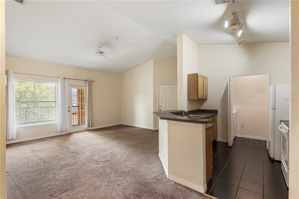 A living room with carpeted floors connects to a kitchen featuring dark countertops and tile — 6025 WESTGATE DRIVE UNIT 2533, ORLANDO, FL