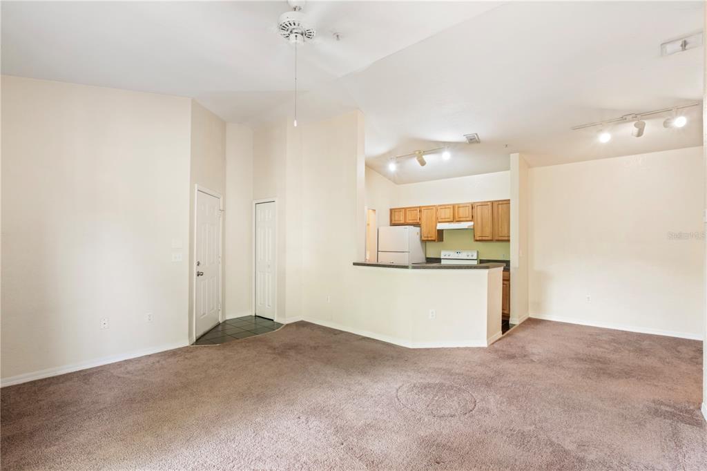 A living room with beige carpet leads to an open kitchen with light wood cabinets — 6025 WESTGATE DRIVE UNIT 2533, ORLANDO, FL