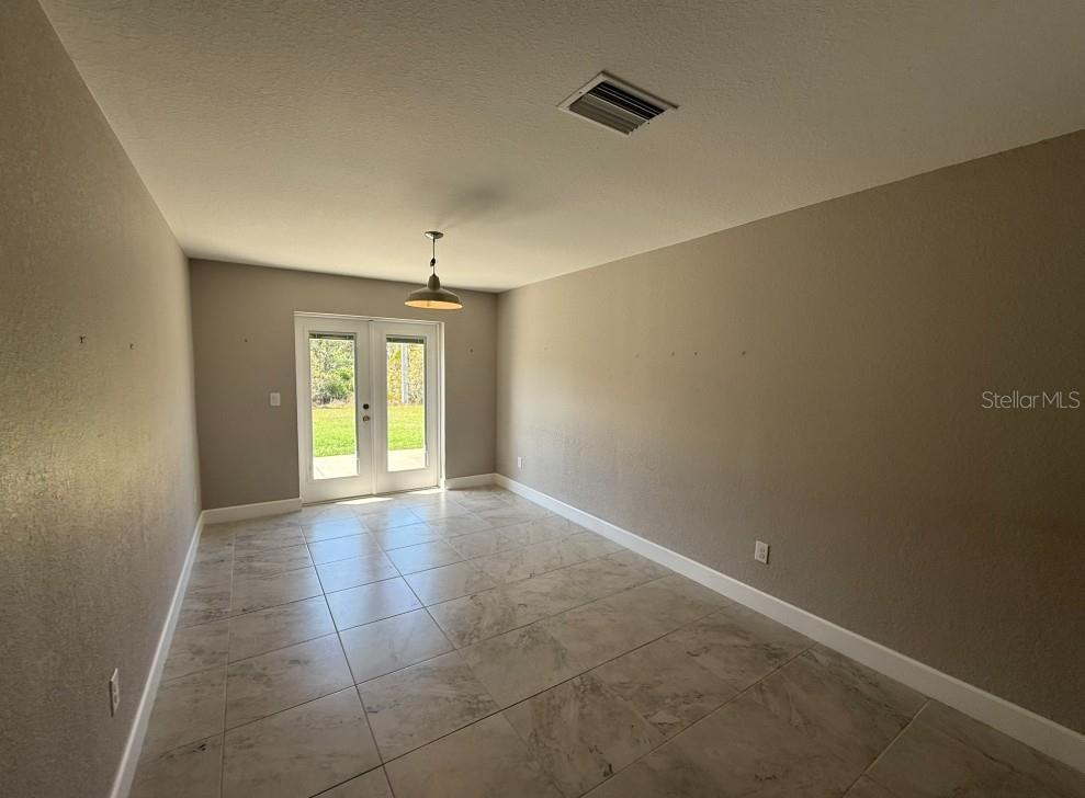 An empty room features light-colored tile flooring, beige walls, a pendant light, and French doors — 113 BOUNDARY BOULEVARD UNIT 2, ROTONDA WEST, FL